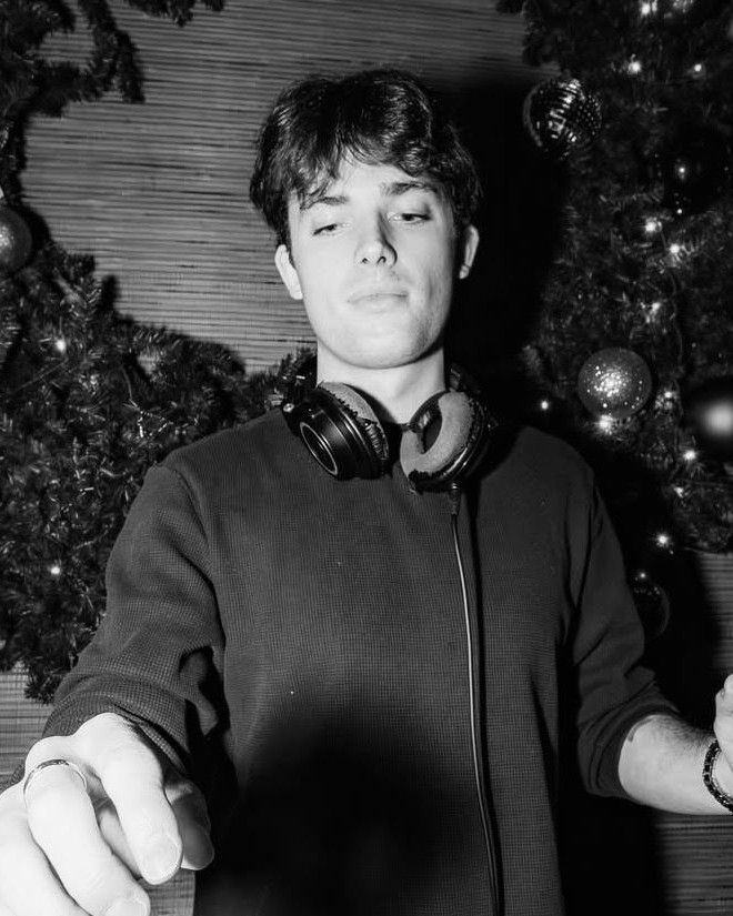LUCOSIS at the decks, headphones around his neck, reaching for the mixer.