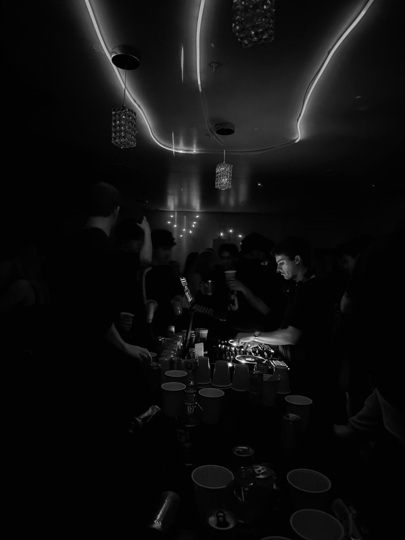 A dark, crowded room, DJs playing behind a table of cups.